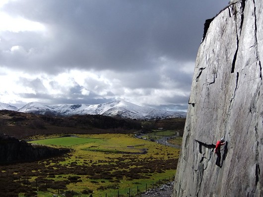 North Wales slate climbing on Solstice (HVS 5a), with the early March snow on the mountains in the background.  © Josh Dickerson
