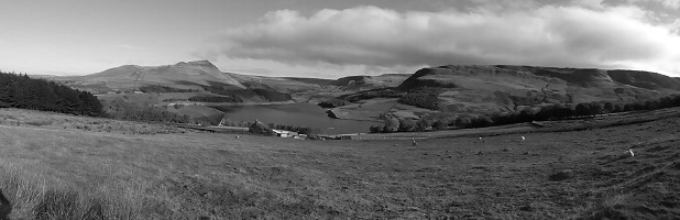 A view of the entrance to Chew Valley. Before 1965 there was no Dovestones Reservoir, just a quiet pastoral valley guarded by the dramatic mountain crag of Alderman on it's left and the foreboding walls of Dovestones Quarry in shadow on the right. Beyond it, the dark battlements of Dovestones Edge rim the moor. In a hidden valley behind, the remote cliffs of Standing Stones and Ravenstones stand over the confluence of Holme and Birchens Cloughs, whilst Charnel Stones are hidden in shadow to the right. Unseen from here but further up Chew Valley are more crags including Rob's Rocks. Almost opposite them, the well named cliffs of Wilderness loom darkly above the upper canyon of Chew Brook. Finally, and not far from this viewpoint, but off-shot to the right, the ominously jutting prows of Wimberry, perhaps the most dramatic crag in the Peak District, dominate the skyline.  © Tony Howard Collection