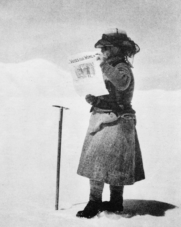 On the Silver Throne Plateau holding a newspaper that reads Votes for Women.  © William Hunter Workman